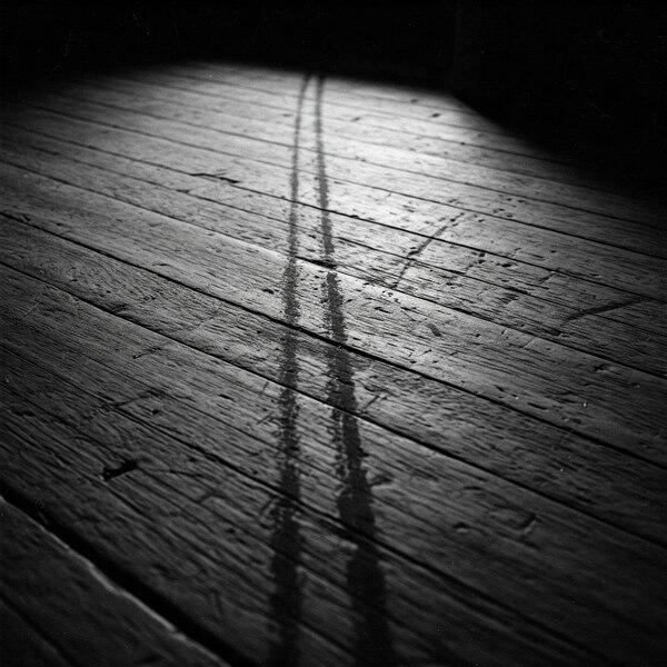 Twin wet trails on wooden attic floorboards, lit by window – symbol of unseen erotic release